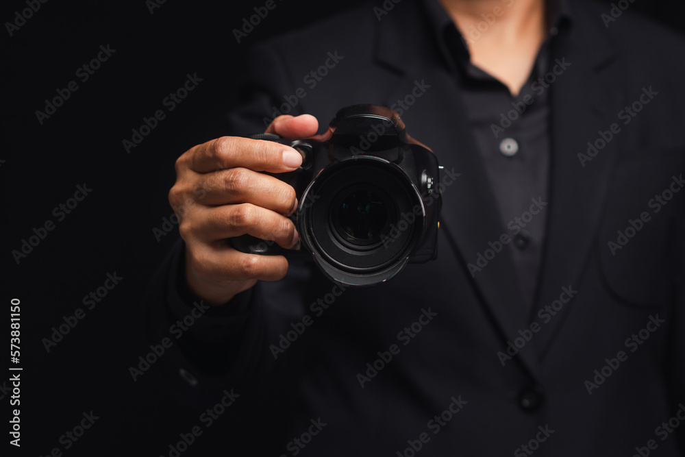 Photographer in a suit holding the digital camera while standing on a black background