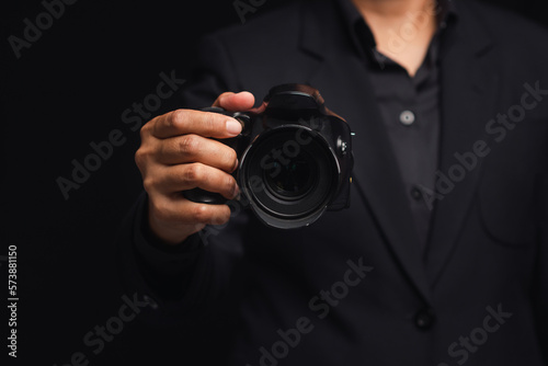 Photographer in a suit holding the digital camera while standing on a black background