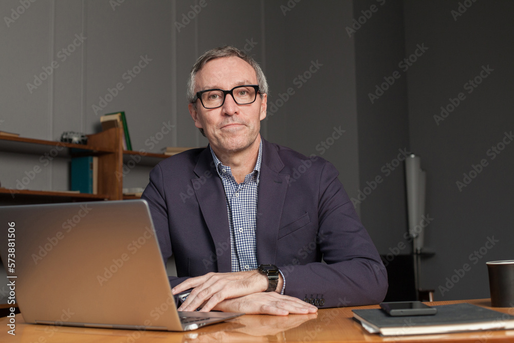 Mature businessman in eye glasses and suit is sitting by the  laptop in office