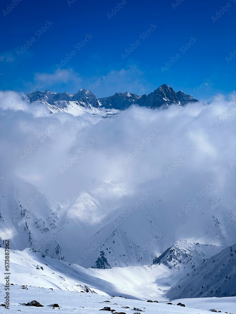 snow covered mountains in winter with stormy clouds touching it. Vibrant blue sky and mountains 