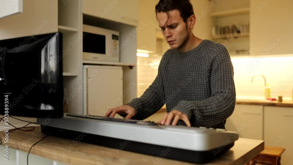 man learns to play the piano synthesizer at home via video link from the Internet, looks at the monitor. man learns to play the piano synthesizer at home via video link from the Internet, looks at the monitor.