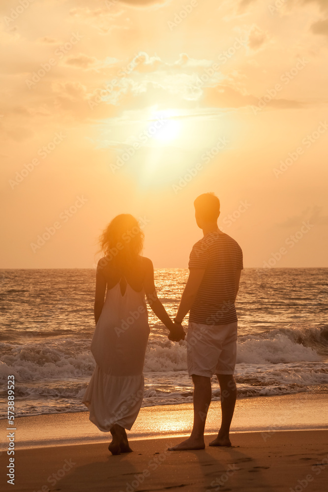 Rear view silhouettes lovely couple in love enjoying honeymoon summer on tropical sandy beach at sunset background. From behind happy couple holding hands. Family travel vacation concept. Copy space