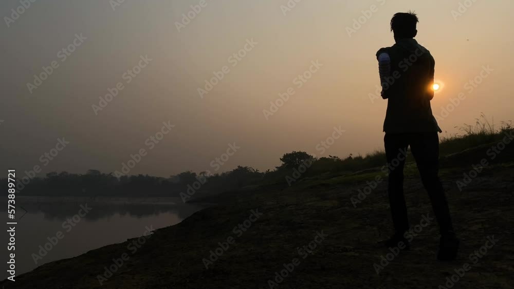 Slow motion rear view of young man jogging towards sun by river, hazy morning Slow motion rear view of young man jogging towards sun by river, hazy morning