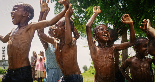 Close Up on a Group of Happy and Innocent Black Children Playing and Enjoying the Blessing of Rain Water After Long Drought. Authentic African Kids Jumping and Laughing when Water Gets Poured on Them.