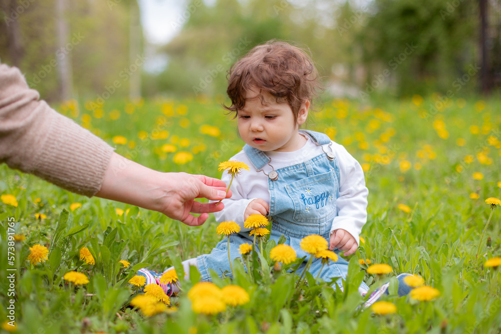 Happy little baby girl sitting on a green meadow with yellow flowers dandelions on the nature in the park Happy little baby girl sitting on a green meadow with yellow flowers dandelions on the nature in the park