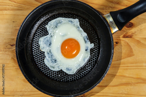 Cooking roasted eggs for breakfast, another egg is driven into pan for fried eggs.