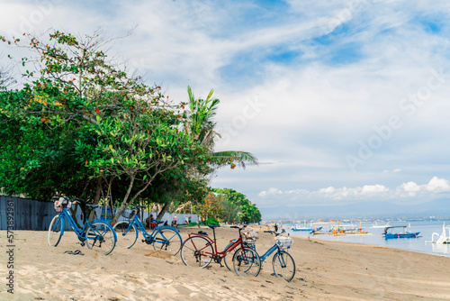 Bicycles for rent on a sandy beach next to the ocean on a background of tropical greenery.