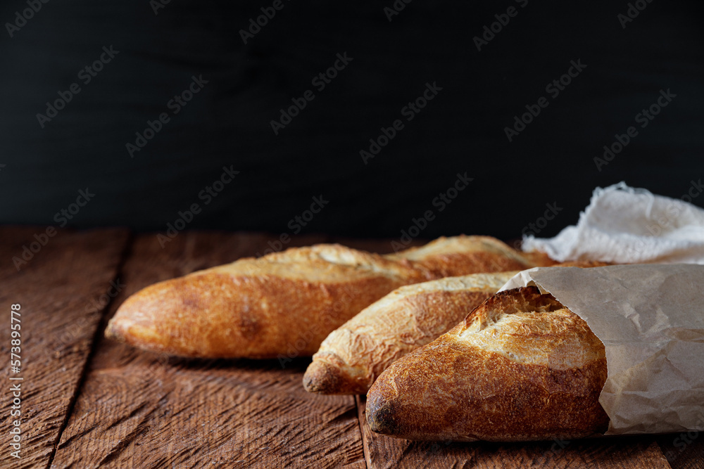 Three rustic baguettes on a wooden table and a dark background close-up
