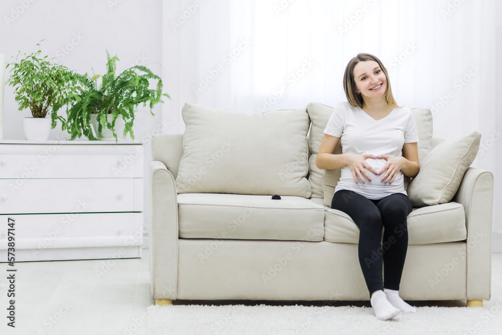 Photo of smiling pregnant woman showing a heart with her fingers on stomach. Photo of smiling pregnant woman showing a heart with her fingers on stomach.