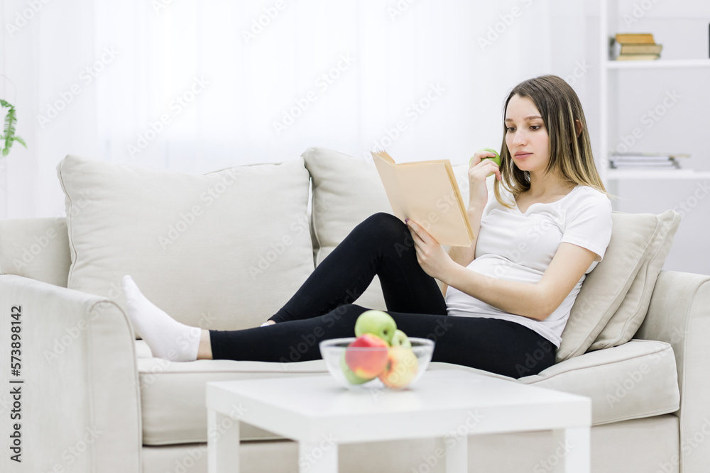 Pregnant woman sitting on sofa and reading a book. Pregnant woman sitting on sofa and reading a book.