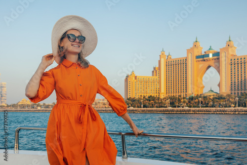 Photography happy elegant woman in orange dress on yacht with Atlantis hotel in background