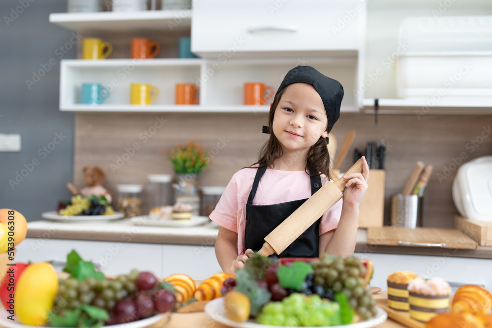 Smile little girl wearing apron holding rolling pin for preparing to make bread and cake bakery in kitchen. Enjoy children learn to make cooking in class room. Smile little girl wearing apron holding rolling pin for preparing to make bread and cake bakery in kitchen. Enjoy children learn to make cooking in class room.
