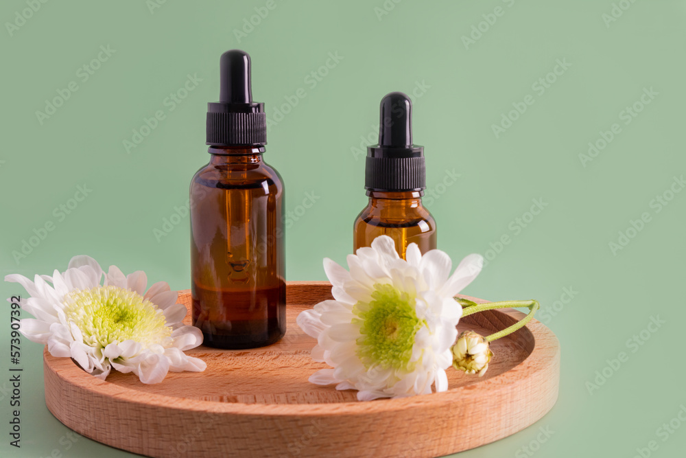 two bottles with a dropper with a natural remedy or serum for organic skin care of the face stand on a wooden plate. front view. green background. two bottles with a dropper with a natural remedy or serum for organic skin care of the face stand on a wooden plate. front view. green background.