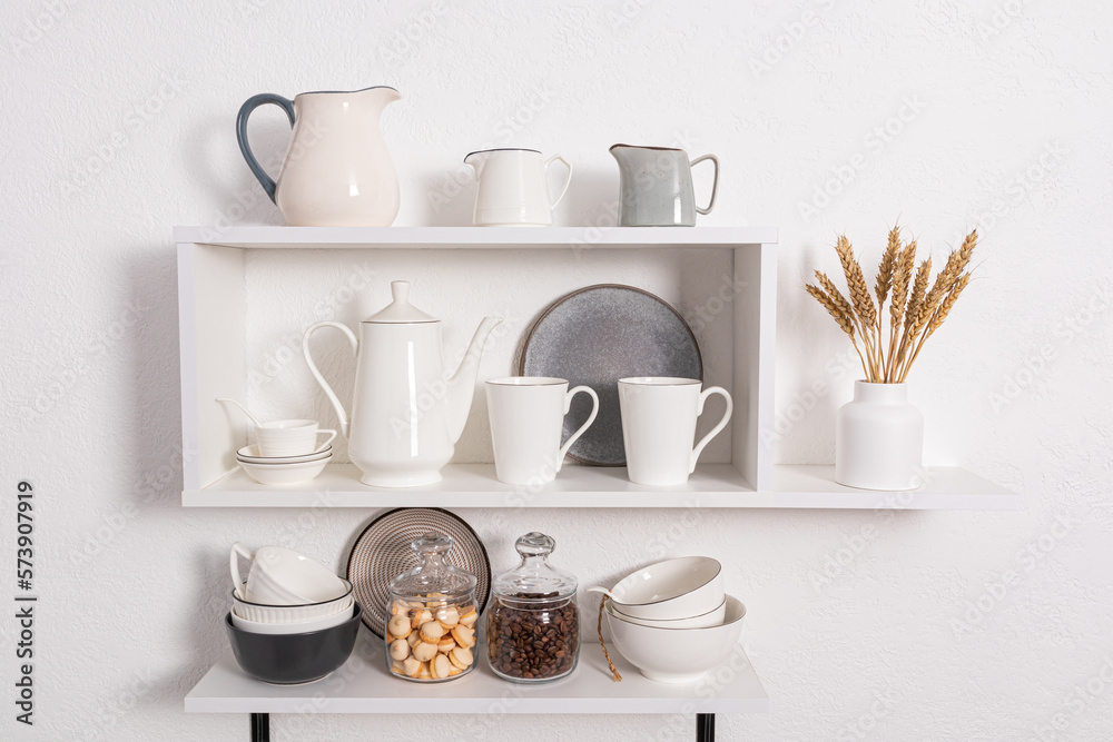 foreground view, close-up of open kitchen shelves with porcelain and ceramic utensils. stylish kitchen background in white tones. foreground view, close-up of open kitchen shelves with porcelain and ceramic utensils. stylish kitchen background in white tones.