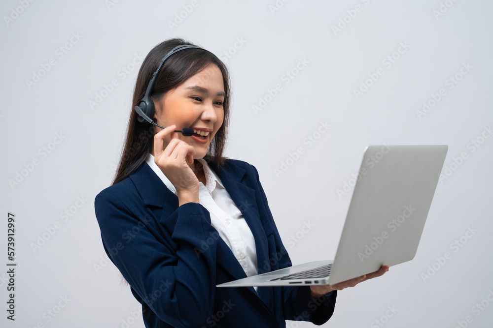 Beautiful Asian call center operator talking with customer using laptop isolated on grey background. Beautiful Asian call center operator talking with customer using laptop isolated on grey background.