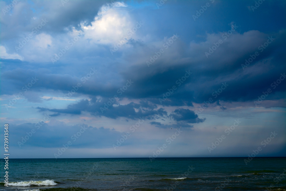 The sea is in front of a thunderstorm. Rain strip over the sea. Clouds in the blue sky