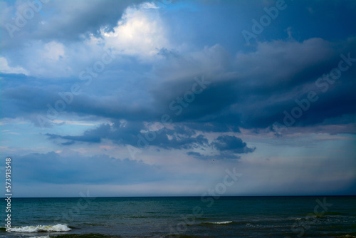 The sea is in front of a thunderstorm. Rain strip over the sea. Clouds in the blue sky © Александр Коваленко