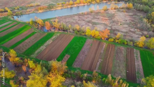 Ploughed and sown fields on agricultural lands on riverside in summer aerial view. Birds eye view on countryside relief and river. Drone flying in sky. Hectares of farmland plots, plant growing.