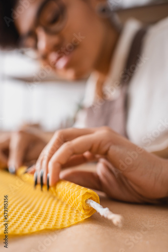 blurred african american woman rolling wax sheet while making candle in craft workshop.