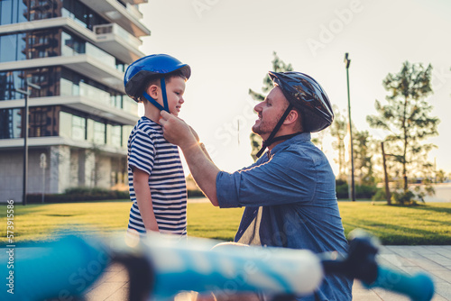 Tela Stock photo of a father helping his son put on a bicycle helmet.