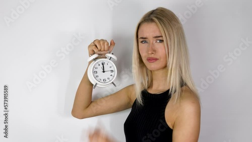An attractive blonde haired woman holding up an old style alarm clock that is set to 12 o'clock, waking up at 12am or 12pm concept, filmed in 4k footage photo