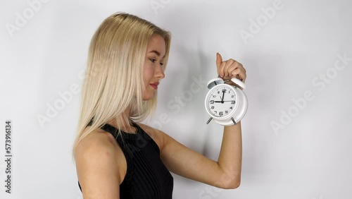 An attractive blonde haired woman holding up an old style alarm clock that is set to 9 o'clock, waking up at 9am or 9pm concept, filmed in 4k footage photo