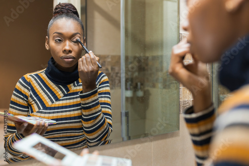 Concentrated young black female applying makeup in bathroom