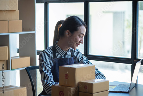 An Asian businesswoman enjoys his online SME business selling products, profiting from opening an online store, and taking orders for customer parcels inside the office. Concept SME Business. © PHAISITSAWAN