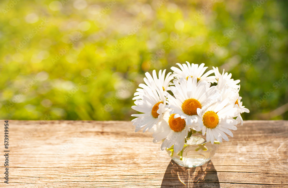 Obraz premium bright sunny background with daisies in a glass on a wooden table top 