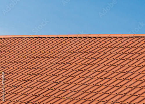 Roof with orange tiles on a background of blue sky. Shingles texture. New roof
