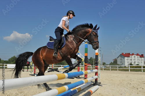 Girl jockey riding a horse jumps over a barrier on equestrian competitions. Girl riding a horse on jumping competitions. © Mykola