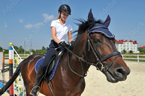 Girl riding bay horse on arena at equestrian school.