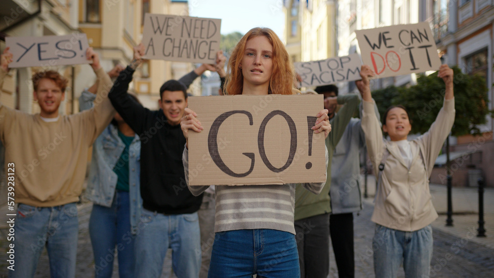 Obraz premium Redhead woman in front shows Go poster protest against racism with students protesting at background