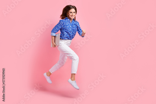 Full length photo of cute impressed woman dressed blue blouse jumping holding device empty space isolated pink color background