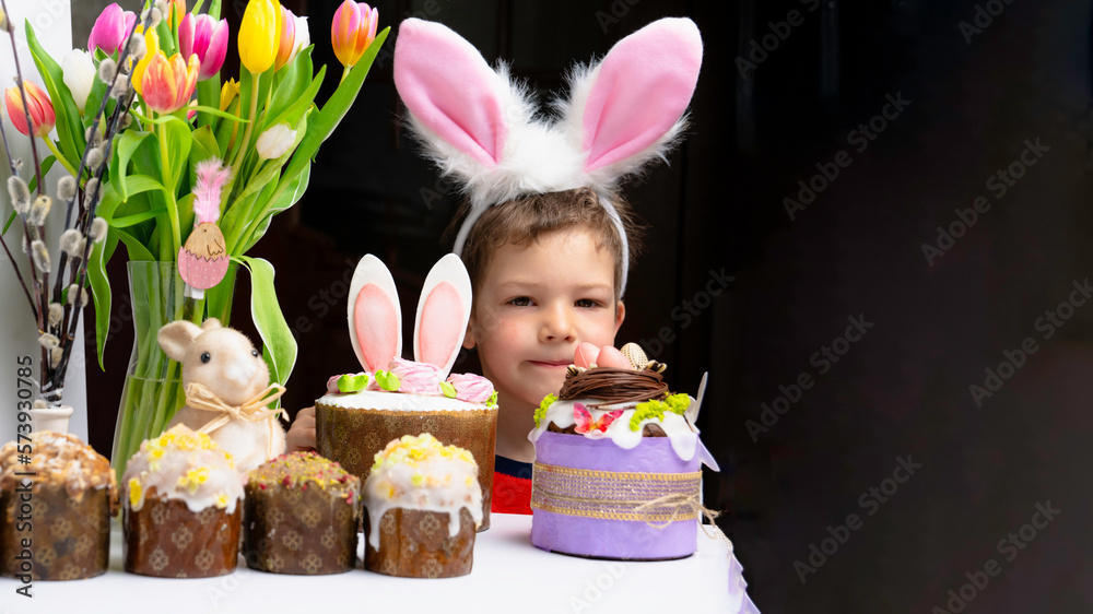 Cute little boy with bunny ears looking at tasty easter sweet cake