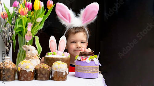 Obraz na płótnie Cute little boy with bunny ears looking at tasty easter sweet cake w salonie