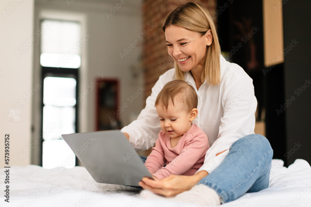 Happy mother and her little daughter using laptop computer at home, woman showing cartoons to toddler child Happy mother and her little daughter using laptop computer at home, woman showing cartoons to toddler child