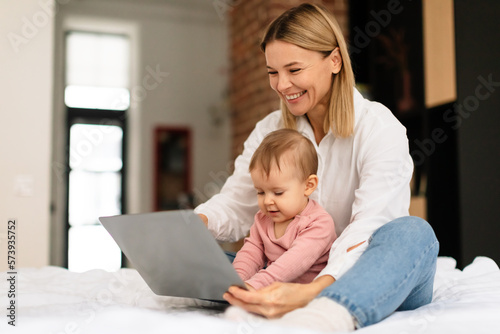 Happy mother and her little daughter using laptop computer at home, woman showing cartoons to toddler child © Prostock-studio