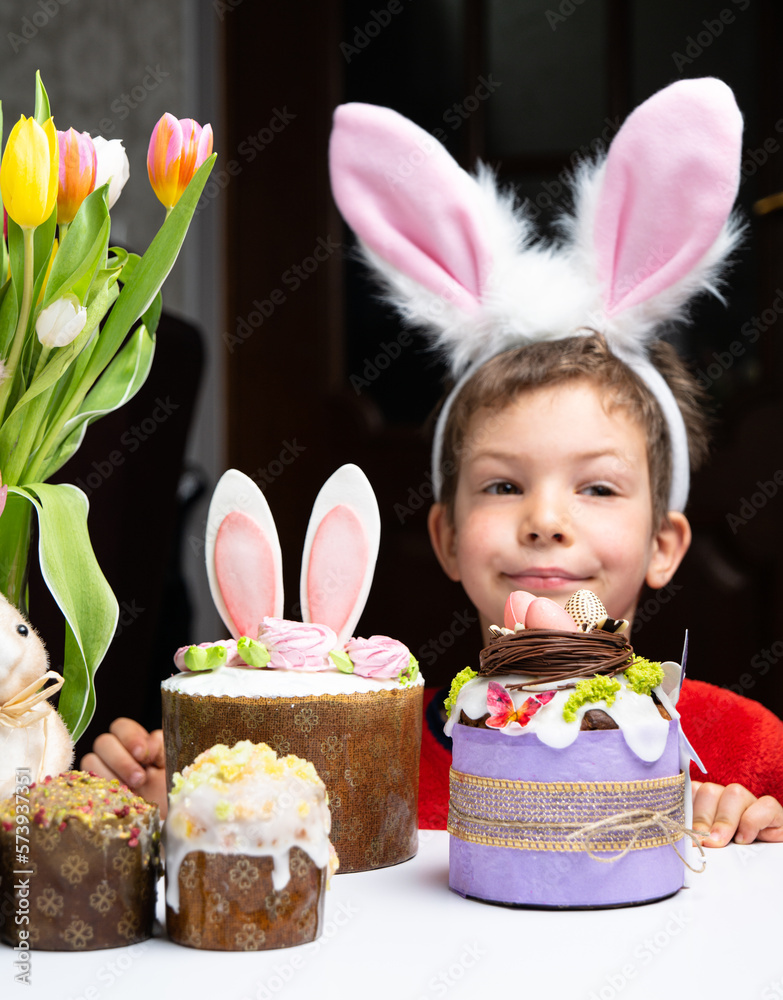 Cute little boy with bunny ears looking at tasty easter sweet cake