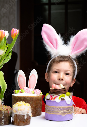 Cute little boy with bunny ears looking at tasty easter sweet cake
