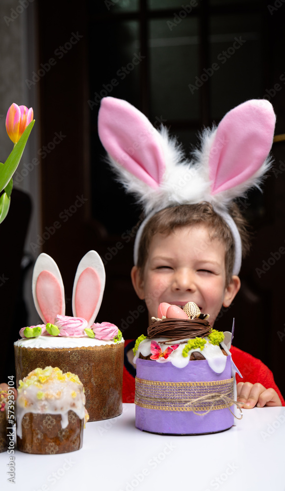 Cute little boy with bunny ears looking at tasty easter sweet cake
