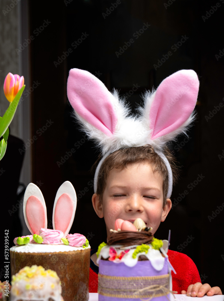 Cute little boy with bunny ears looking at tasty easter sweet cake