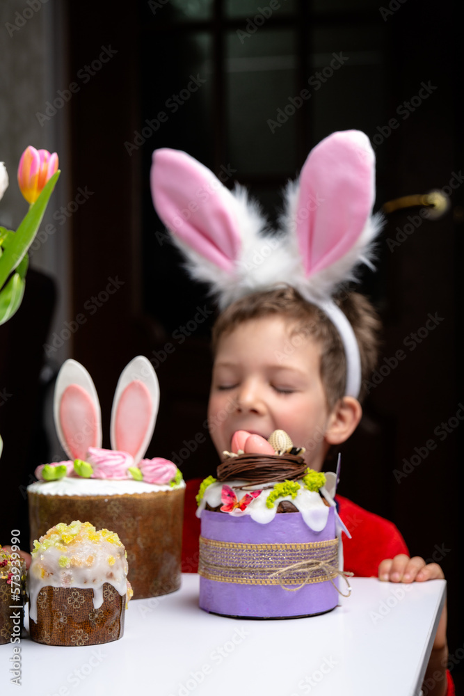 Cute little boy with bunny ears looking at tasty easter sweet cake