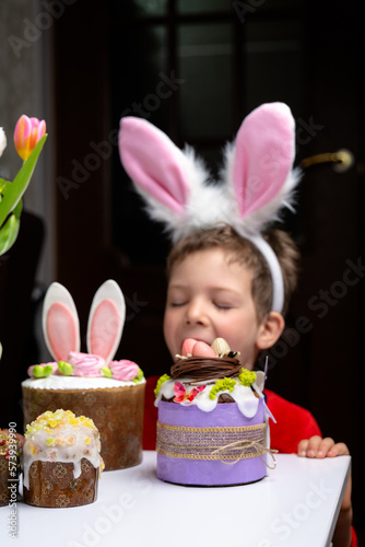 Obraz na płótnie Cute little boy with bunny ears looking at tasty easter sweet cake w salonie