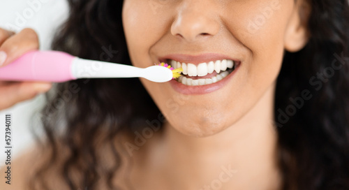 Glad happy millennial caucasian brunette female brushing white teeth with electric modern toothbrush
