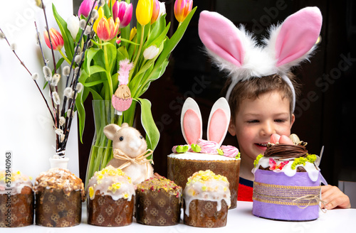 Obraz na płótnie Cute little boy with bunny ears looking at tasty easter sweet cake w salonie