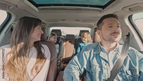 Happy lovely family traveling together by car having fun. Attractive handsome happy dad driving with pretty young wife and two kids. Little girl sitting in baby car seat having fun with brother.