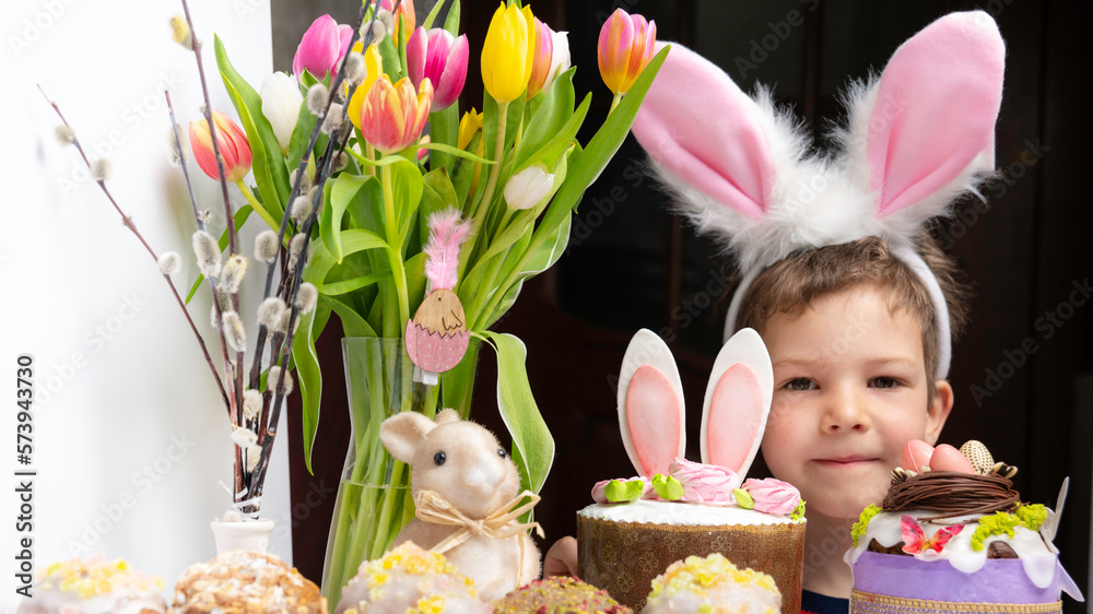 Cute little boy with bunny ears looking at tasty easter sweet cake