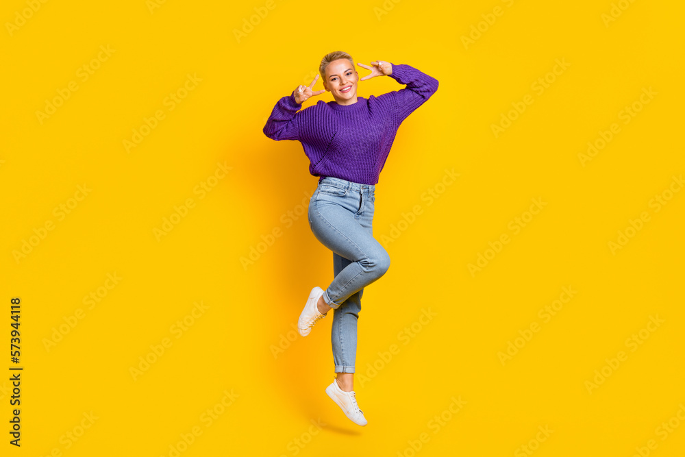 Full size photo of excited carefree girl jumping show v-sign have good mood isolated on yellow color background