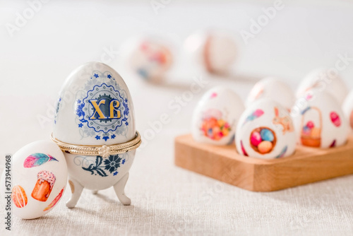 A large egg-box with the inscription XB and Easter eggs on a linen tablecloth on the table. The concept of the Bright Easter holiday.